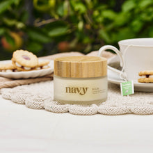 Load image into Gallery viewer, Jar of &#39;navy&#39; balm on a table with a cup of tea and cookies