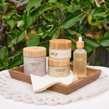 Load image into Gallery viewer, Navy skincare products on a wooden tray with greenery in the background