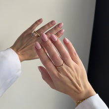 Load image into Gallery viewer, A close-up of a person's hands with neatly manicured light pink nails, wearing gold rings and a gold bracelet, dressed in a white long-sleeve top against a neutral light gray background.