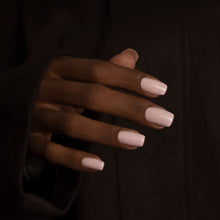 Load image into Gallery viewer, A close-up of a hand with neatly manicured, square-shaped nails painted in a soft pale pink, set against a dark brown textured background.