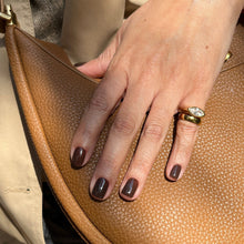 Charger l'image dans la galerie, A close-up of a hand with dark brown manicured nails resting on a tan pebbled leather handbag, wearing a gold ring.