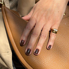 Load image into Gallery viewer, A close-up of a hand with dark brown manicured nails resting on a tan pebbled leather handbag, wearing a gold ring.