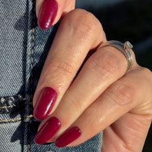 Load image into Gallery viewer, A close-up of a hand with glossy deep berry red manicured nails, wearing a silver ring and resting against a blue denim jacket.
