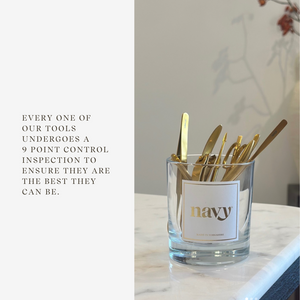 Glass container with gold utensils labeled 'Navy' on a marble surface.