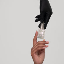 Charger l'image dans la galerie, A hand wearing a black glove reaches for a small clear bottle held by another hand, against a plain light gray background.