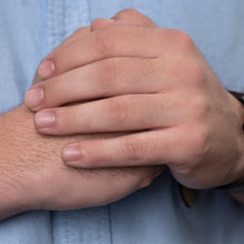 Load image into Gallery viewer, A close-up shot of a man's hands clasped together on his chest, wearing a light blue button-down shirt and a silver-toned wristwatch with a dark face.