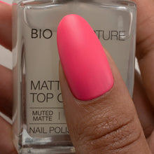 Load image into Gallery viewer, A close-up of a hand holding a bottle of BIO NATURE MATTED MATTE nail polish, with the pink polish swatch shown on a fingernail.