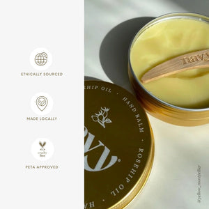 Hand balm in a tin with a wooden applicator on a light background, featuring ethical sourcing and local manufacturing details.